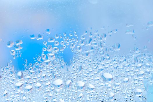 Wet glass with large drops of water or rain of blue color. Background or wallpaper with water texture close-up. Image of water droplets on a clear glass surface during heavy rain