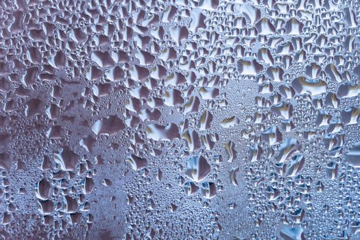 Wet glass with large drops of water or rain of blue color. Background or wallpaper with water texture close-up. Image of water droplets on a clear glass surface during heavy rain