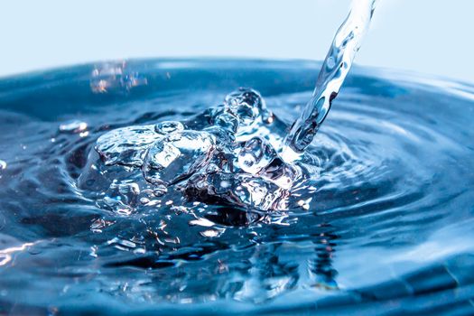 A flowing stream of blue water. Splash of water close-up. Frozen water drop photographed at high speed.Slow dripping of liquid with air bubbles. Nature backgrounds or Wallpaper.Frozen liquid splashes