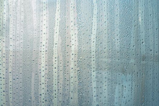 Wet glass with large drops of water or rain of blue color. Background or wallpaper with water texture close-up. Image of water droplets on a clear glass surface during heavy rain