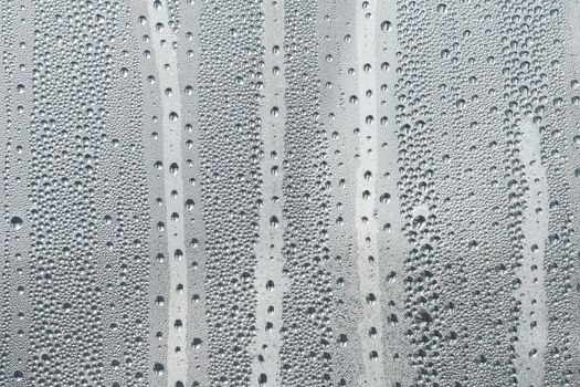 Abstract background ornament with water drops.Raindrops on the glass in rainy weather.The glittering, shiny surface of water on glass.Water drops in the form of balls or spheres.Grey raindrops