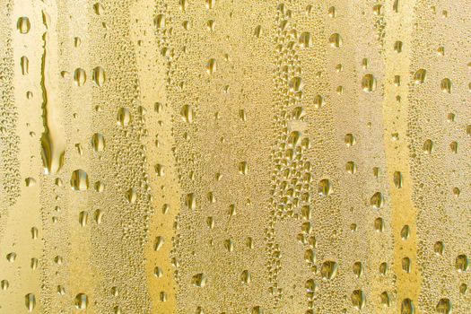 Abstract background ornament with golden water drops.Raindrops are golden in color.Sparkling shiny water surface on the glass.Water drops in the form of balls or spheres.Colored raindrops