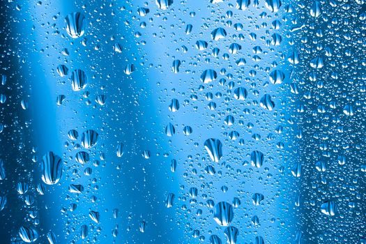 Abstract background ornament with water drops.Raindrops on the glass in rainy weather.The glittering, shiny surface of water on glass.Water drops in the form of balls or spheres.Blue raindrops