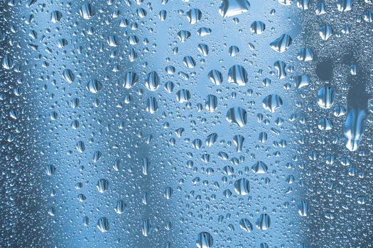 Raindrops on the glass in rainy weather.The glittering, shiny surface of water on glass.Water drops in the form of balls or spheres.Blue raindrops background. Abstract backgrounds ornament with water