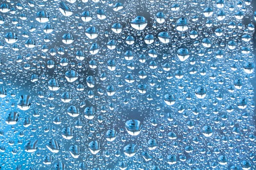 Abstract background ornament with blue water drops.Raindrops are blue in color.Sparkling shiny water surface on the glass.Water drops in the form of balls or spheres.Colored raindrops backdrop