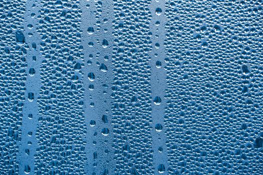 Raindrops on the glass in rainy weather.The glittering, shiny surface of water on glass.Water drops in the form of balls or spheres.Blue raindrops background. Abstract backgrounds ornament with water