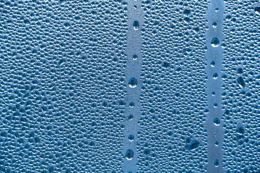 Abstract background ornament with water drops.Raindrops on the glass in rainy weather.The glittering, shiny surface of water on glass.Water drops in the form of balls or spheres.Blue raindrops