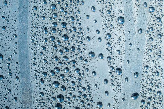 Abstract background ornament with water drops.Raindrops on the glass in rainy weather.The glittering, shiny surface of water on glass.Water drops in the form of balls or spheres.Blue raindrops