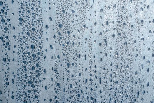 Abstract background ornament with water drops.Raindrops on the glass in rainy weather.The glittering, shiny surface of water on glass.Water drops in the form of balls or spheres.Blue raindrops