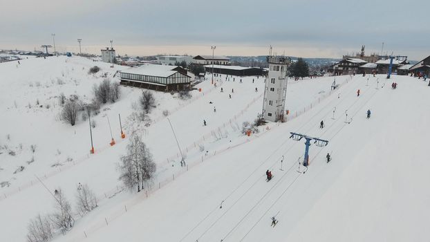 Aerial view: Skiers and snowboarders going down the slope in winter day. Skiers and snowboarders enjoying on slopes of ski resort in winter season.