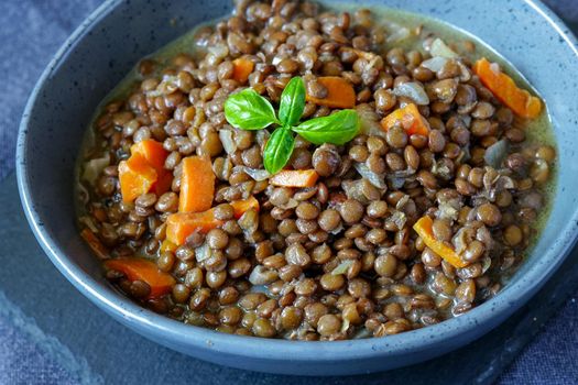 Lentil porridge in a ceramic bowl on the table. Close-up shot. The food is decorated with a sprig of Basil.