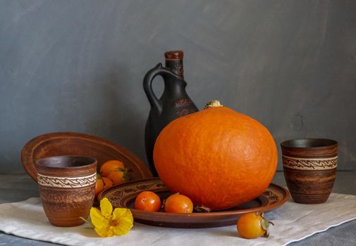 Autumn still life with pumpkin and nasturtium flowers. On the table there is a ceramic tableware and a tablecloth made of natural materials.