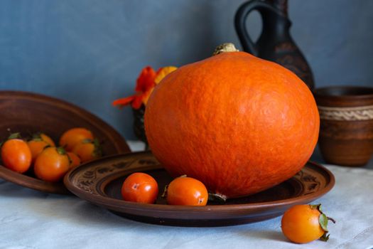 Autumn still life with pumpkin and nasturtium flowers. On the table there is a ceramic tableware and a tablecloth made of natural materials.