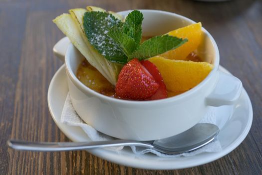 Caramel dessert with fresh fruits in a snow-white porcelain Cup on a wooden table.