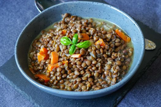 Lentil porridge in a ceramic bowl on the table. Close-up shot. The food is decorated with a sprig of Basil.