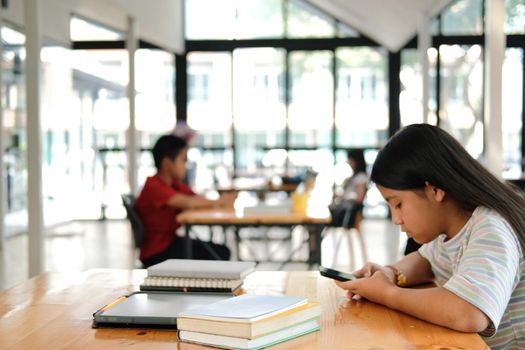 asian girl student using social media online app on smart mobile phone in library