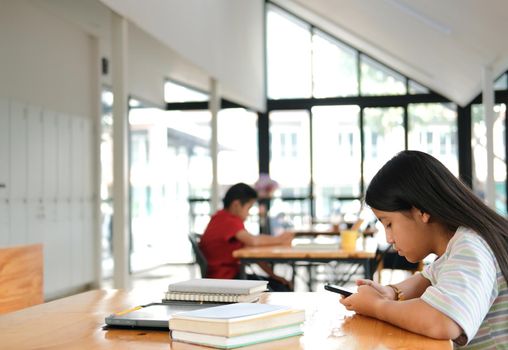 asian girl student using social media online app on smart mobile phone in library