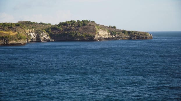 Rocky coast with high cliffs, sea surf with breaking waves on the coast, Nusa Penida, Indonesia. Ocean with waves and rocky cliff. Travel concept.