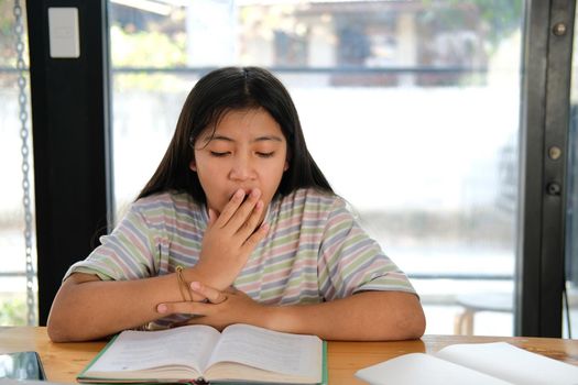 asian girl student yawning while reading book feeling tired bored sleepy. children education