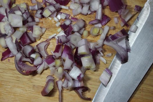 Chopped white onion with sharp knife on wooden cutting board. High angle top view of chopped onions pieces