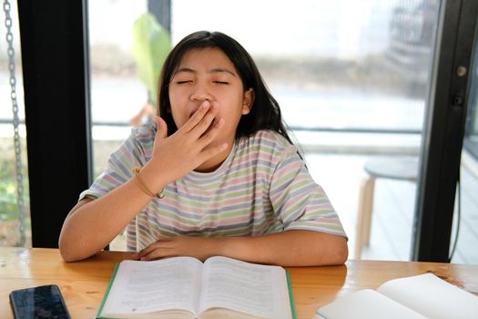 asian girl student yawning while reading book feeling tired bored sleepy. children education