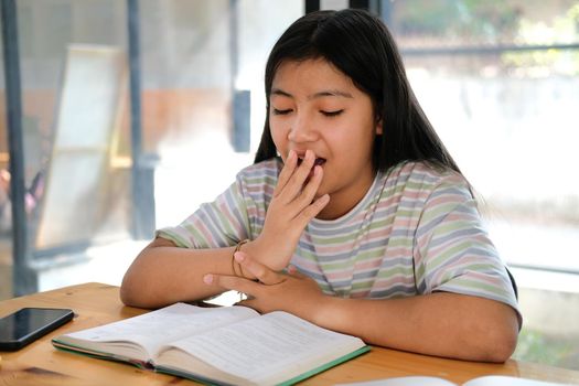 asian girl student yawning while reading book feeling tired bored sleepy. children education