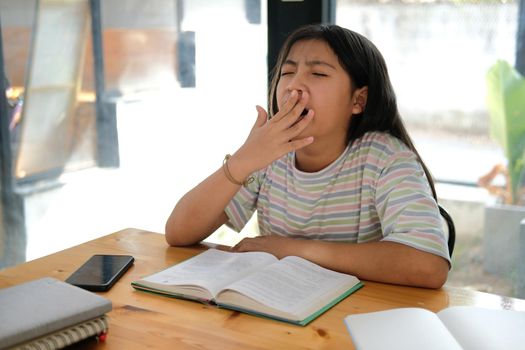 asian girl student yawning while reading book feeling tired bored sleepy. children education