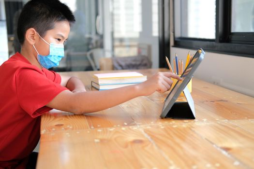 asian boy student wearing face mask studying learning lesson online. remote meeting distance education at home