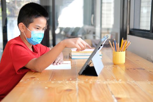 asian boy student wearing face mask studying learning lesson online. remote meeting distance education at home
