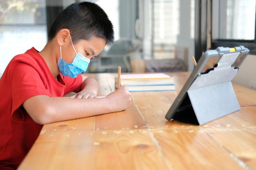 asian boy student wearing face mask studying learning lesson online. remote meeting distance education at home