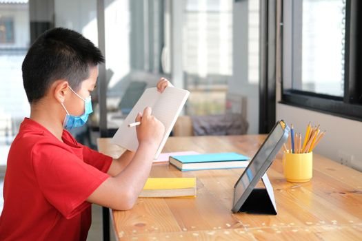 asian boy student wearing face mask studying learning lesson online. remote meeting distance education at home