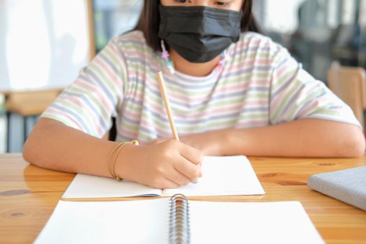 asian girl student wearing face mask studying writing notes doing homework in library. learning education at school