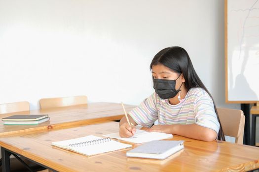 asian girl student wearing face mask studying writing notes doing homework in library. learning education at school
