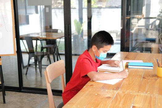 asian boy student wearing face mask studying writing notes doing homework in library. learning education at school