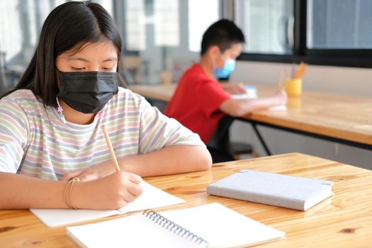 asian girl student wearing face mask studying writing notes doing homework in library. learning education at school