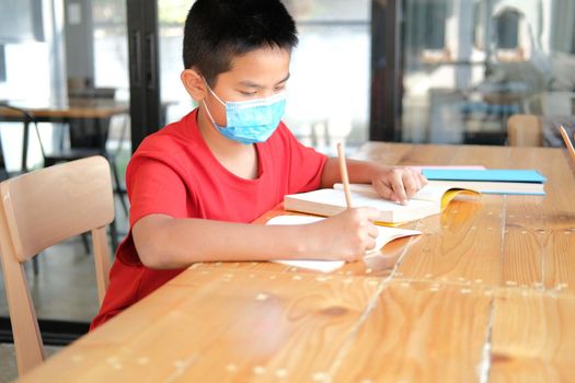 asian boy student wearing face mask studying writing notes doing homework in library. learning education at school