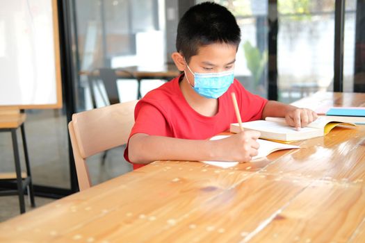 asian boy student wearing face mask studying writing notes doing homework in library. learning education at school