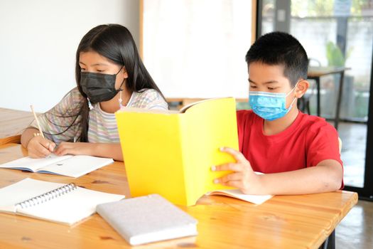 asian girl boy student wearing face mask studying writing notes doing homework in library. learning education at school