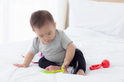 Portrait of cute little baby girl sitting with cozy on bed at bedroom, happiness of toddler, newborn 6-11 months with innocence and expression with cheerful, child charm, indoors, one person.