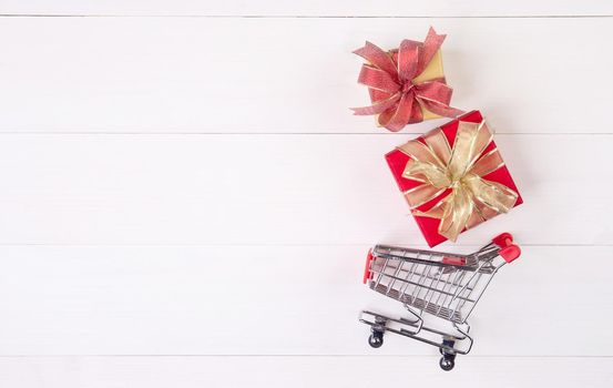 Cart of supermarket and gift box on wooden table, shopping online for presents in valentine day, trolley for sale commerce in holiday and vacation, copy space, celebration and anniversary concept.