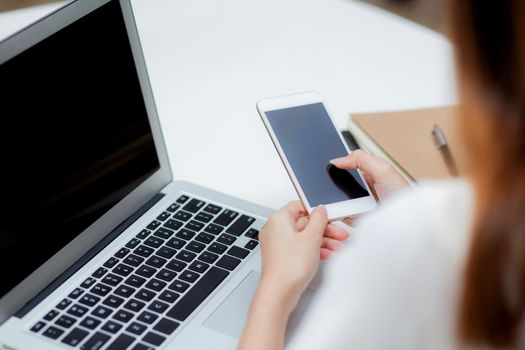 Hand of young woman working with laptop computer and smartphone mockup on desk at home, notebook and phone display blank screen, freelance look message to internet, business and communication concept.