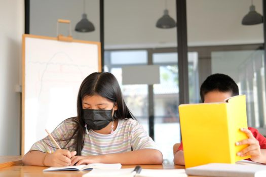 asian girl boy student wearing face mask studying writing notes doing homework in library. learning education at school