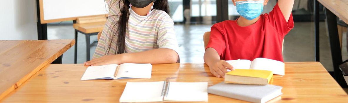 asian girl boy student wearing face mask studying raising hand in classroom. learning education at school