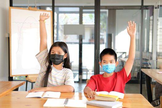 asian girl boy student wearing face mask studying raising hand in classroom. learning education at school