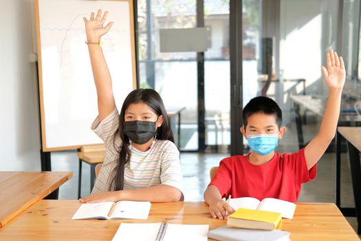 asian girl boy student wearing face mask studying raising hand in classroom. learning education at school