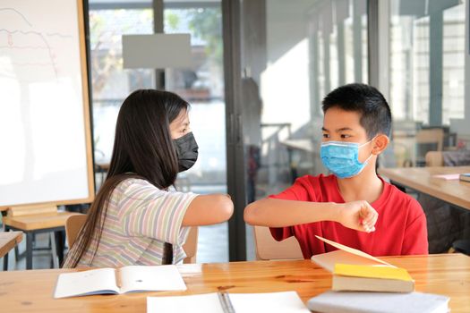 asian girl boy student friends wearing face mask greeting bumping elbow at school. new normal in covid pandemic outbreak