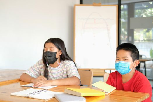 asian girl boy student wearing face mask studying writing notes doing homework in library. learning education at school