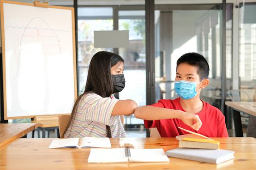 asian girl boy student friends wearing face mask greeting bumping elbow at school. new normal in covid pandemic outbreak