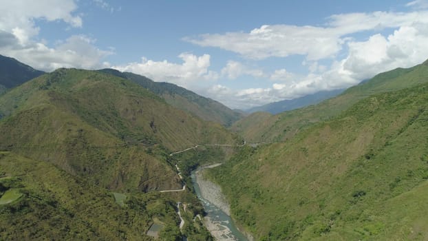Aerial view of mountain river in the cordillera, road on the slopes, mountains covered forest, trees. Cordillera region. Luzon, Philippines. Mountain landscape in cloudy weather.