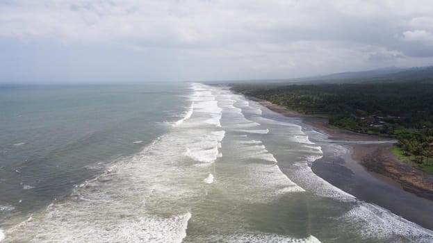 Tropical beach at cloudy weather. Aerial view of big waves on the beach with volcanic black sand in windy weather, Bali. Seascape Ocean, sky, sea. Travel concept.